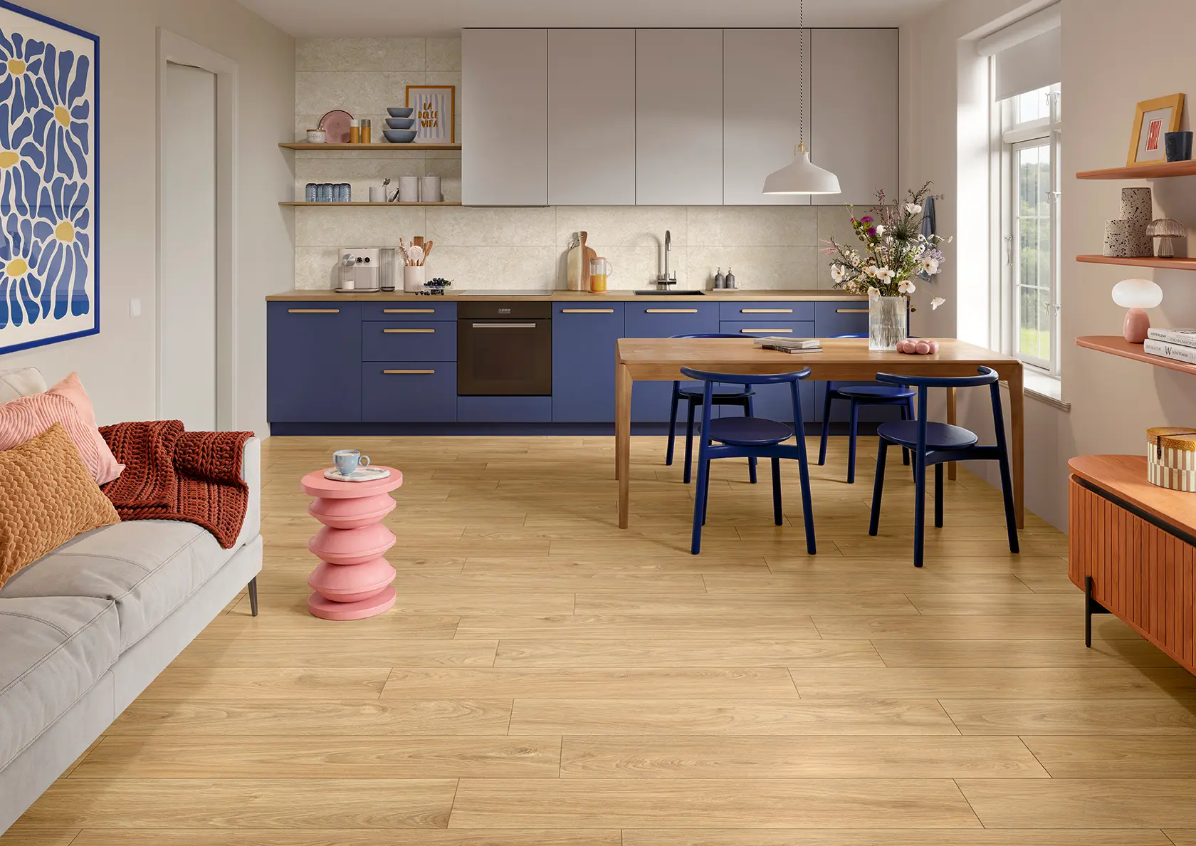 Modern kitchen with blue cabinets, wooden dining table with chairs, and a living area with sofa and pink side table.