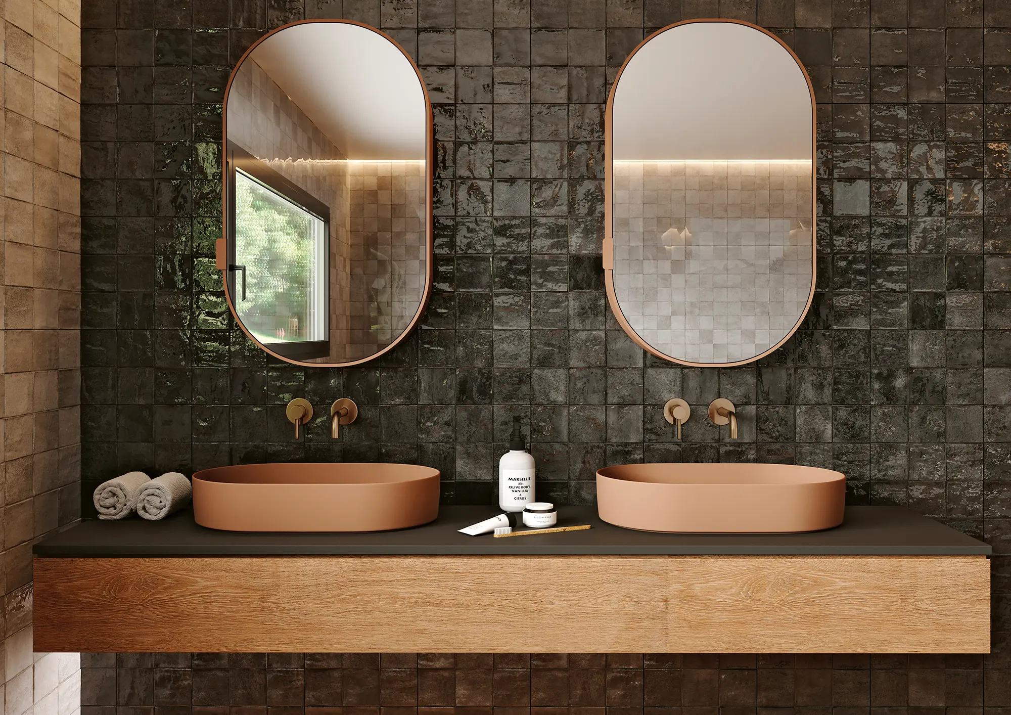 Modern bathroom with dual oval mirrors, brown sinks, dark tiled wall, wooden vanity, and toiletries.