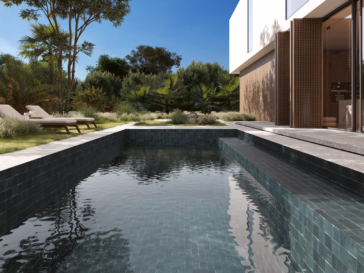 Modern outdoor pool with dark tiles, adjacent lounge chairs, greenery, and a building with wooden shutters.