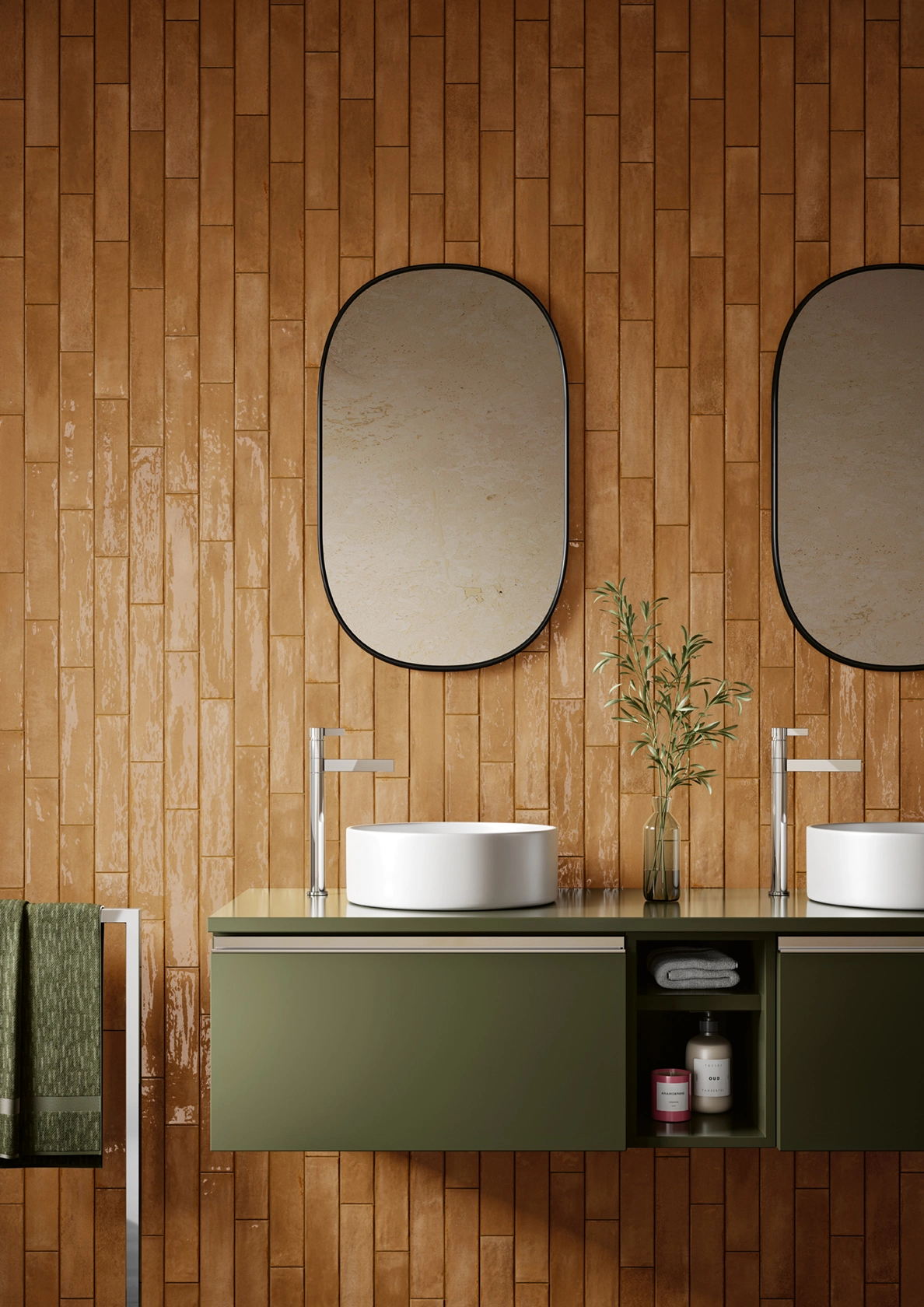 Modern bathroom with two round white sinks on olive green floating vanity and oval mirrors on brown tiled wall.