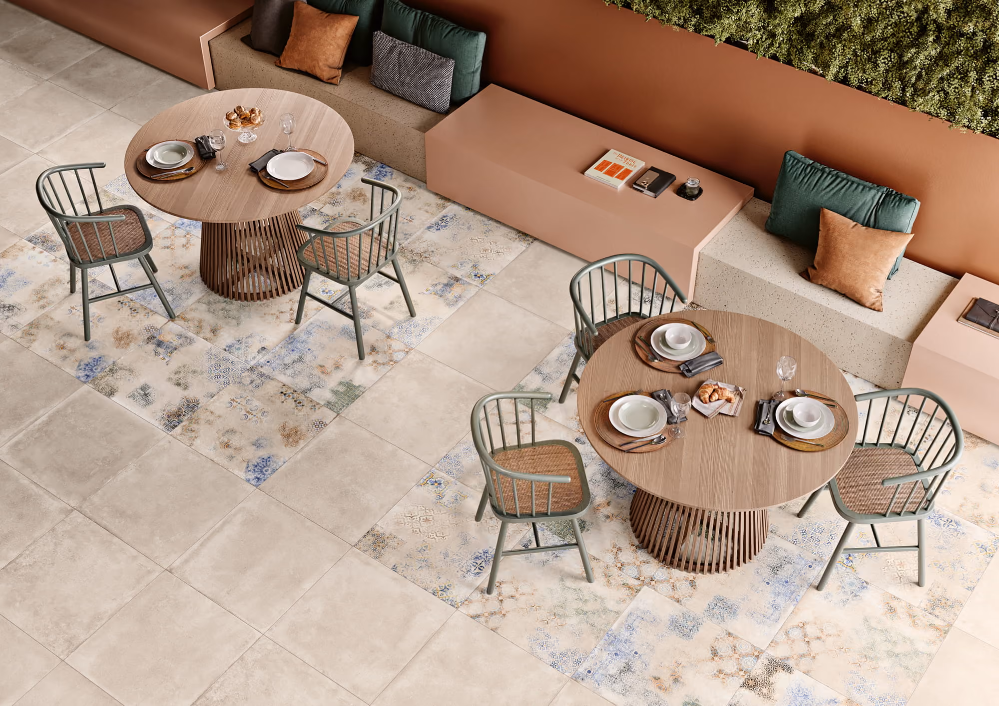 Two round wooden tables with dish settings and green chairs on patterned and beige tile floor.