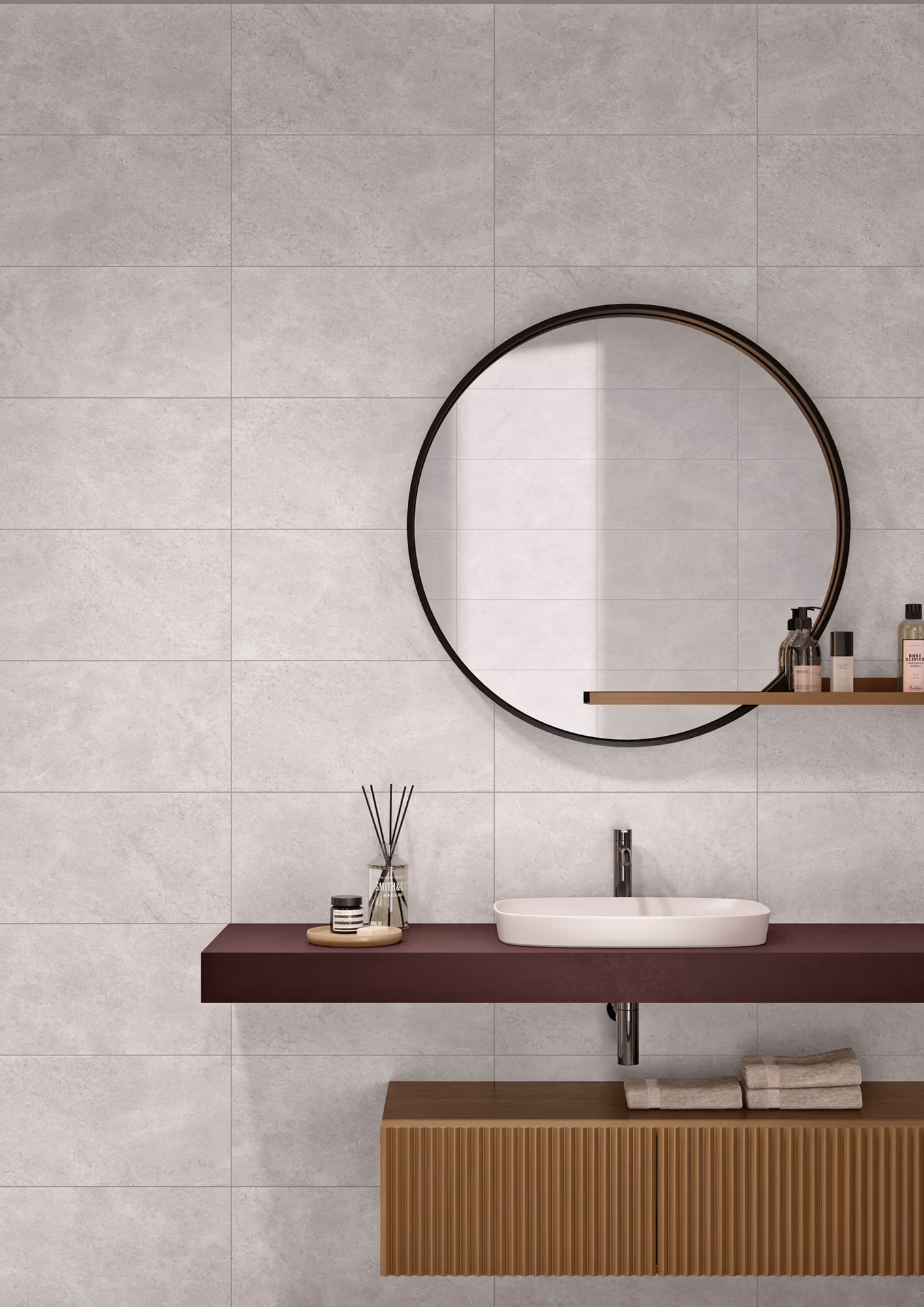 Minimalistic bathroom with round mirror, white sink on dark countertop, toiletries, and folded towels.