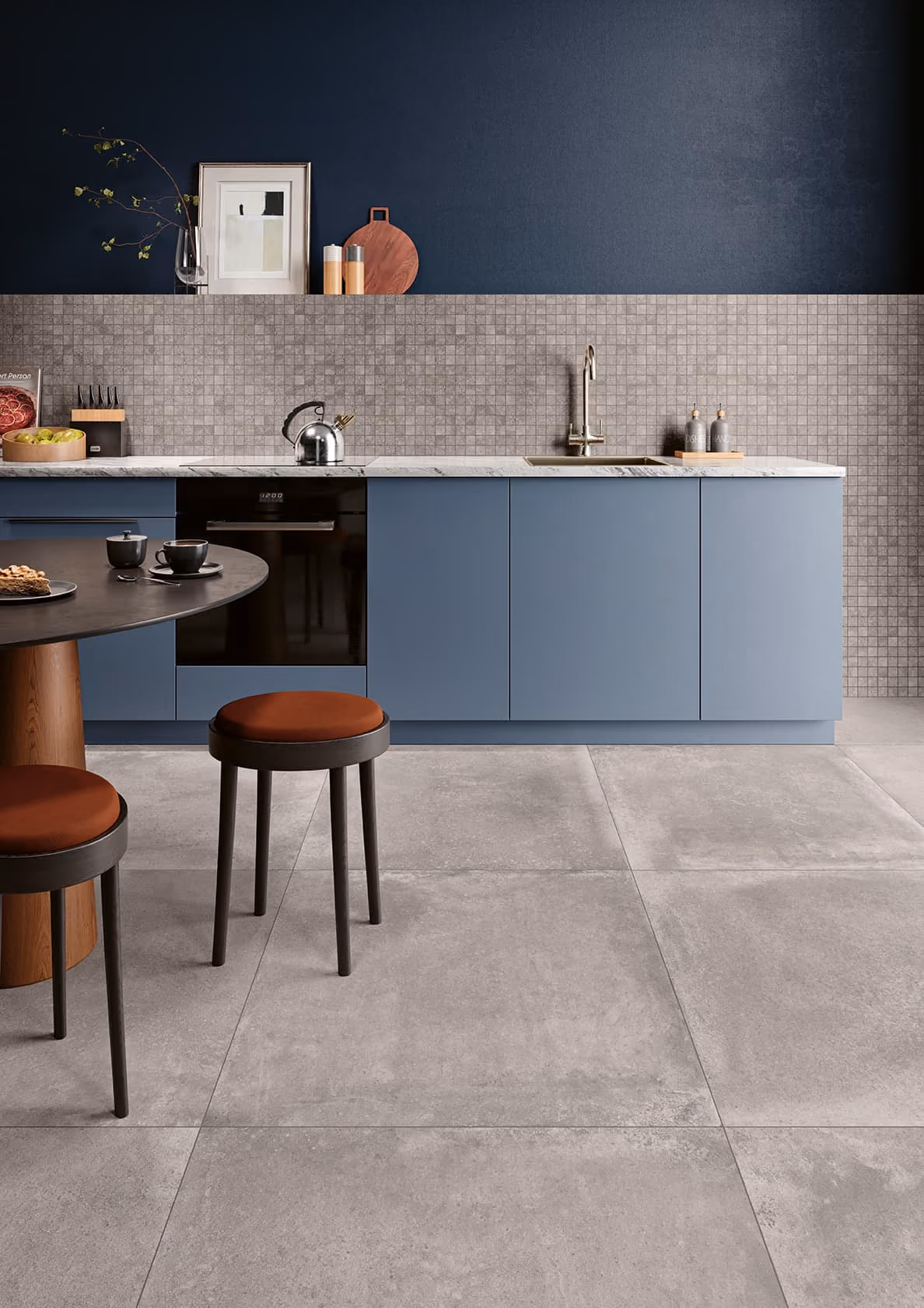 Modern kitchen with blue cabinets, mosaic tile backsplash, round table, and two stools with brown seats.