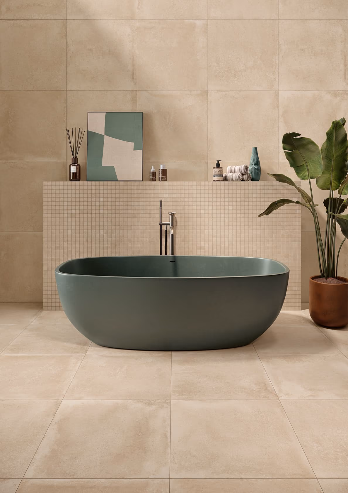 Modern bathroom with green freestanding tub, beige tiled walls, art, toiletries, and a potted plant.