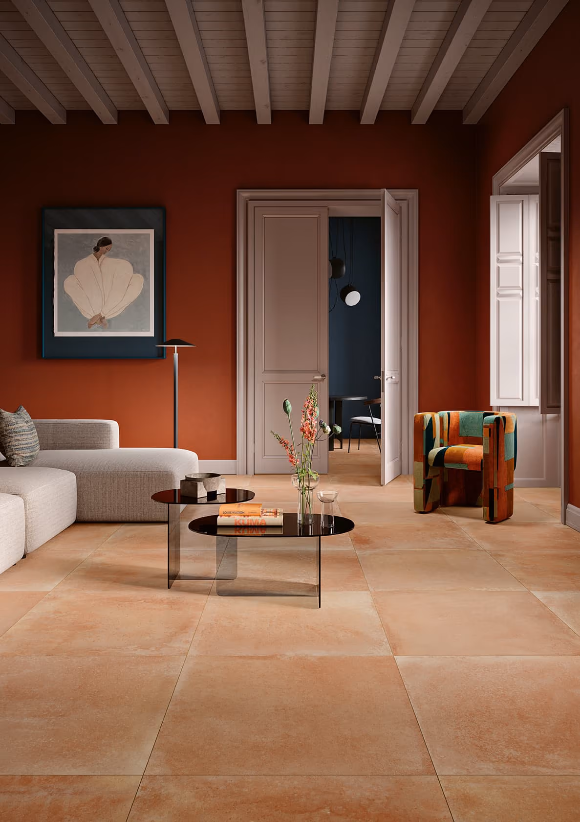 Living room with terracotta walls, light sofa, patterned armchair, glass coffee tables, and a floral painting.
