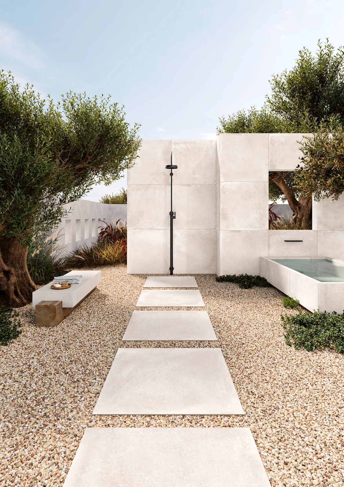Outdoor shower area with large white tiles, gravel ground, bench with towels, and a pool.
