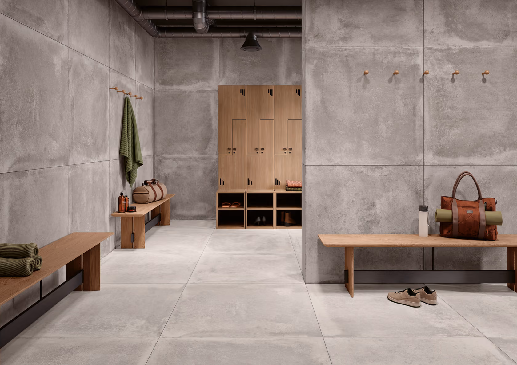 Modern locker room with concrete walls, wooden benches, lockers, towels, bags, and shoes on the floor.
