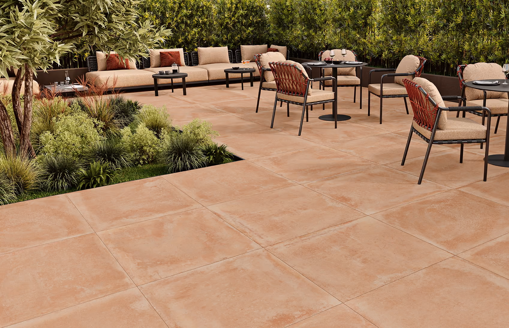 Outdoor patio with beige tiled floor, cushioned chairs, black tables, and green shrubbery.