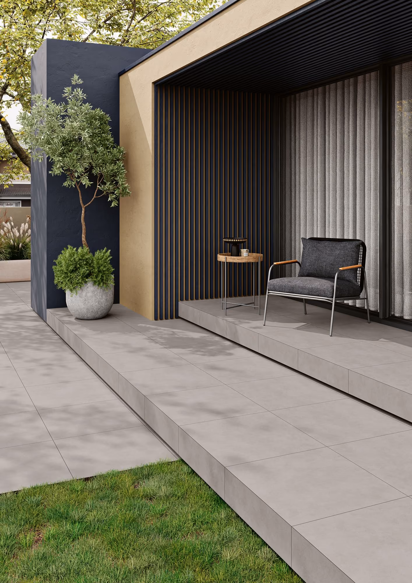 Modern patio with gray tiled floor, a potted tree, small side table, and a gray cushioned chair.