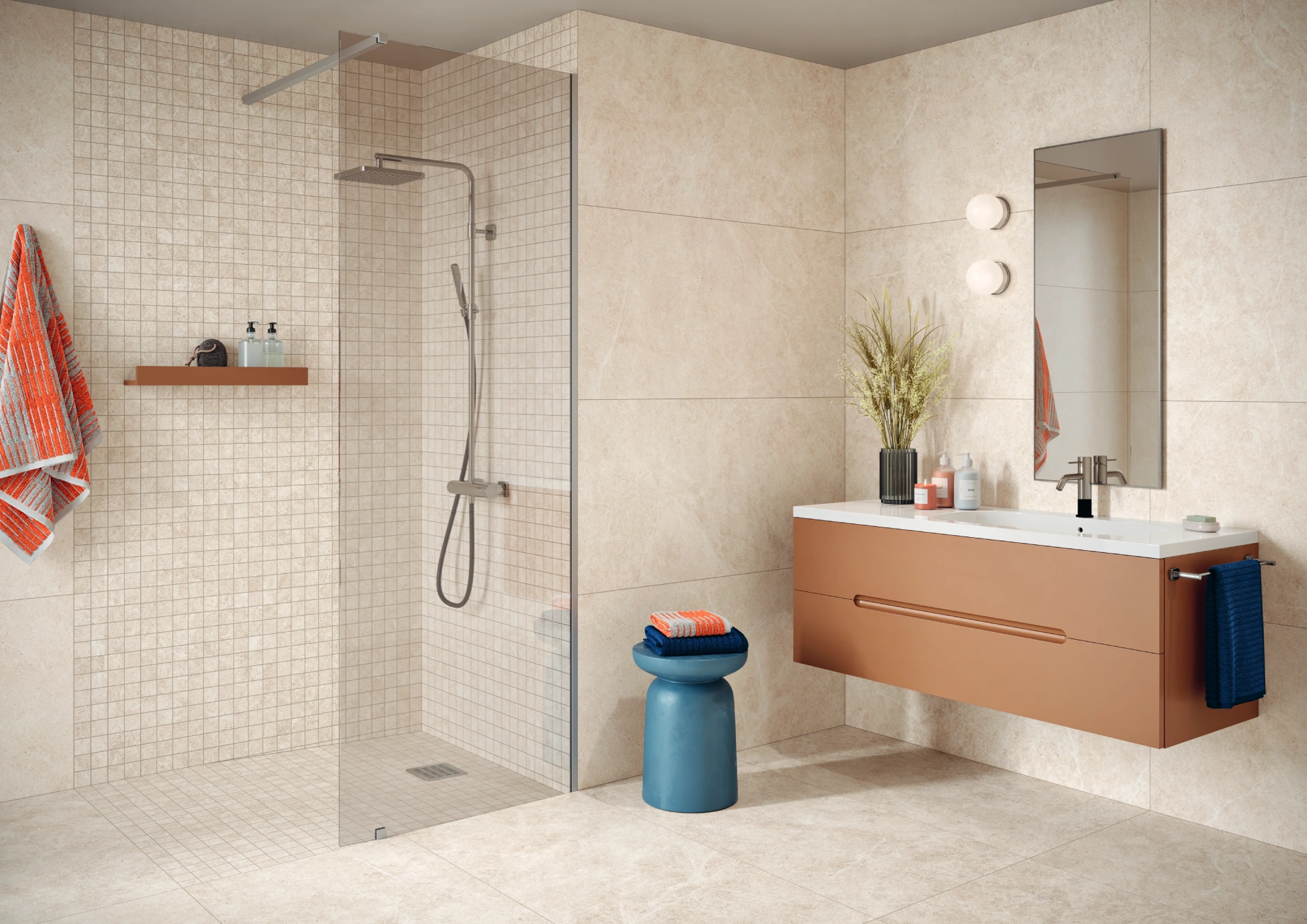 Modern bathroom with walk-in shower, beige tiles, floating vanity, blue stool, and colorful towels.