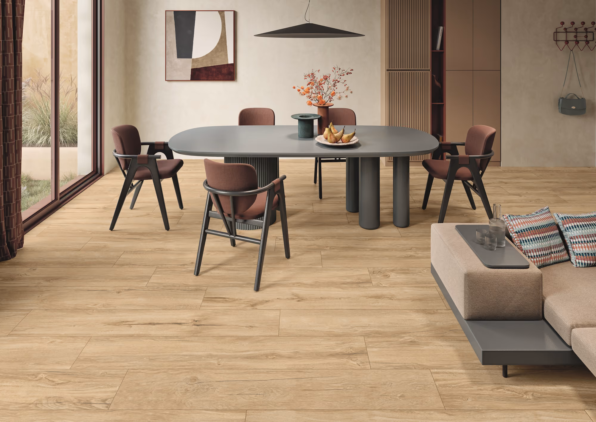 Modern dining room with gray oval table, six brown chairs, wood floor, and beige sofa with cushions.