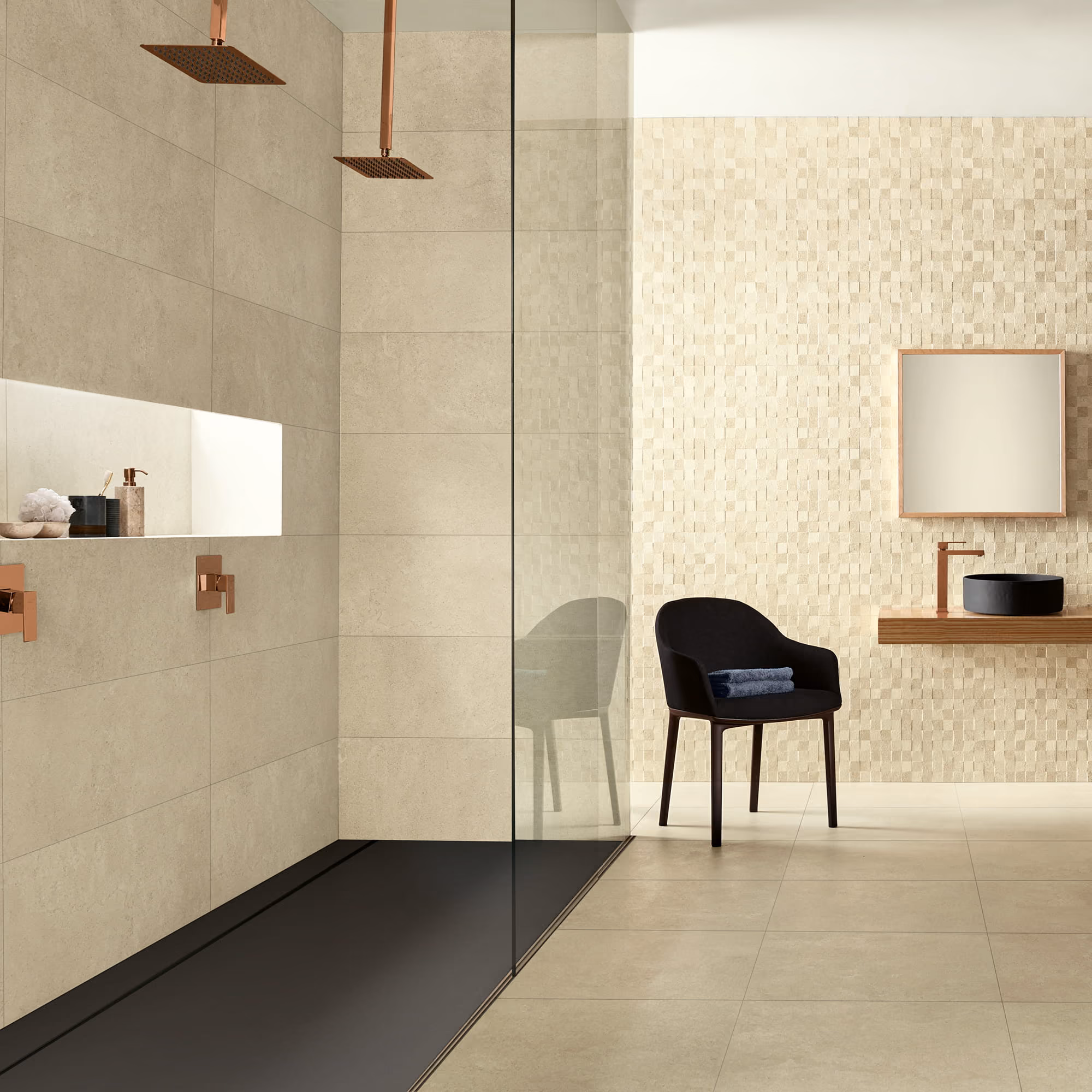 Modern beige bathroom with walk-in shower, copper showerheads, black chair, and floating vanity with round sink.