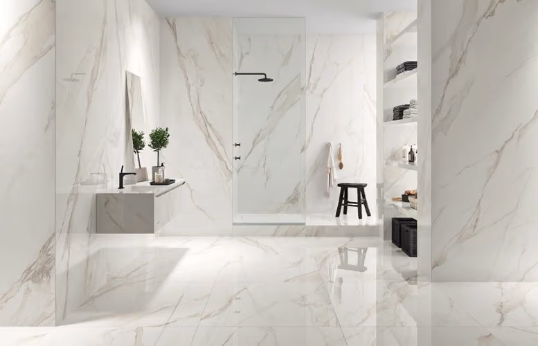 Modern bathroom with white marble walls and floor, glass shower, floating sink, and black stool.