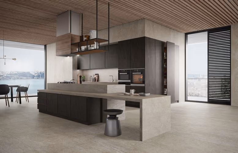 Modern kitchen with dark cabinets, marble island, wooden ceiling, and large windows facing a water view.