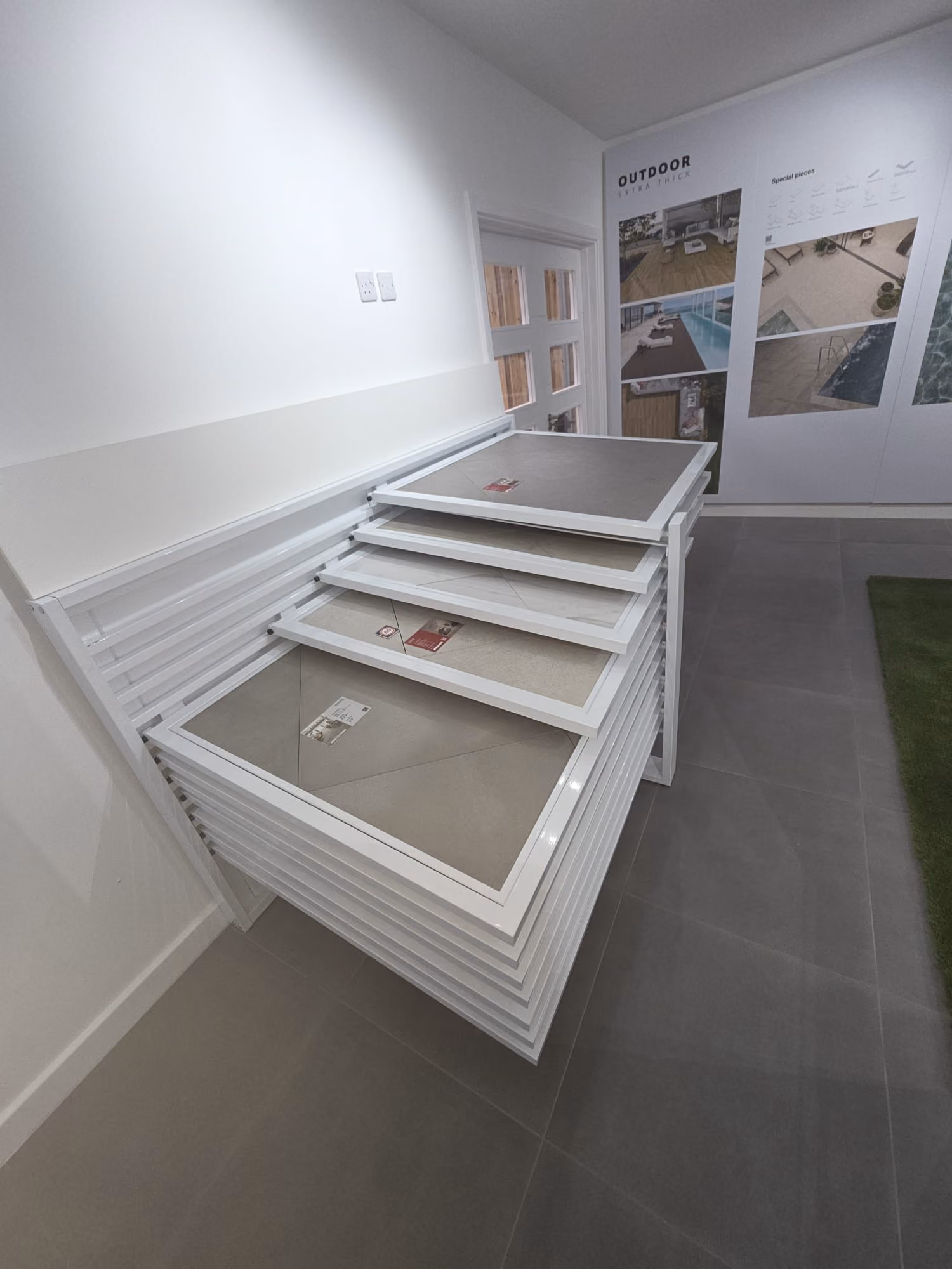 Display rack with large tile samples in a showroom with outdoor tile photos on the wall.