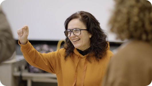 Woman with glasses smiling and gesturing enthusiastically in a casual setting.