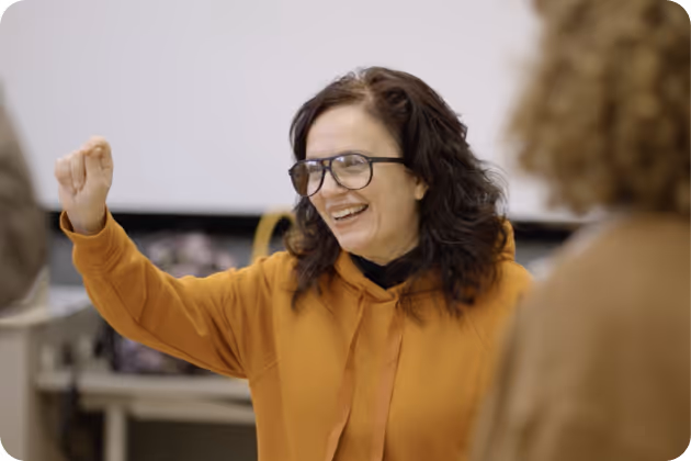 Woman with glasses smiling and gesturing enthusiastically in a casual setting.