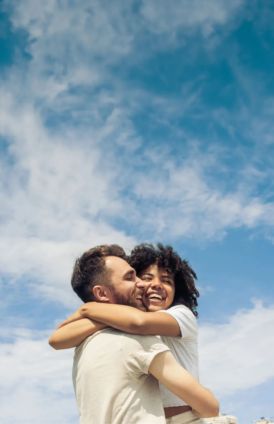 Two people hugging each other with a blue sky and clouds in the background