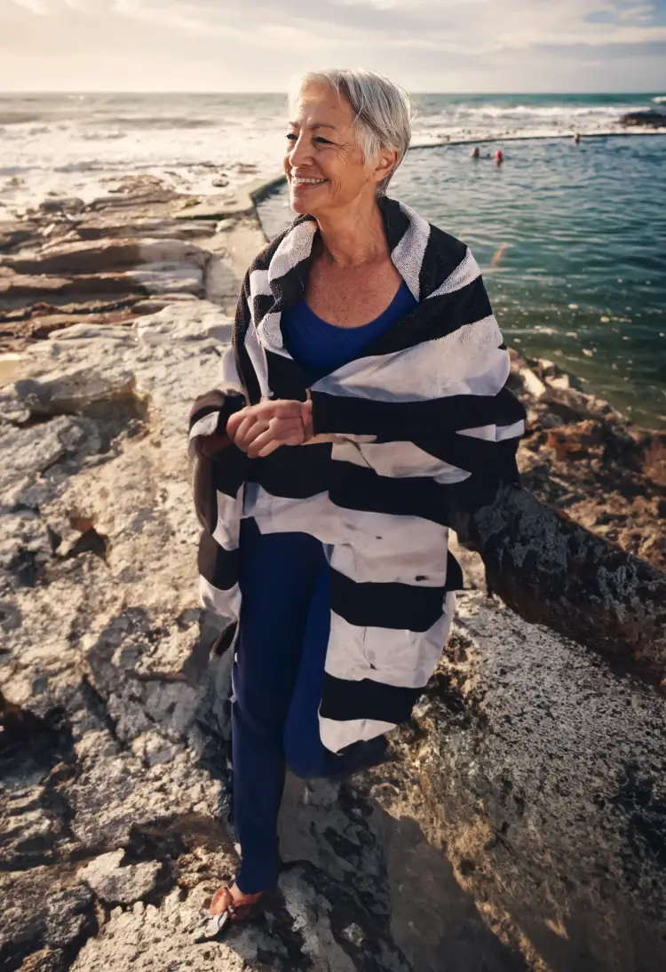 An elderly women looking out into the ocean with a swimming pool behind her.
