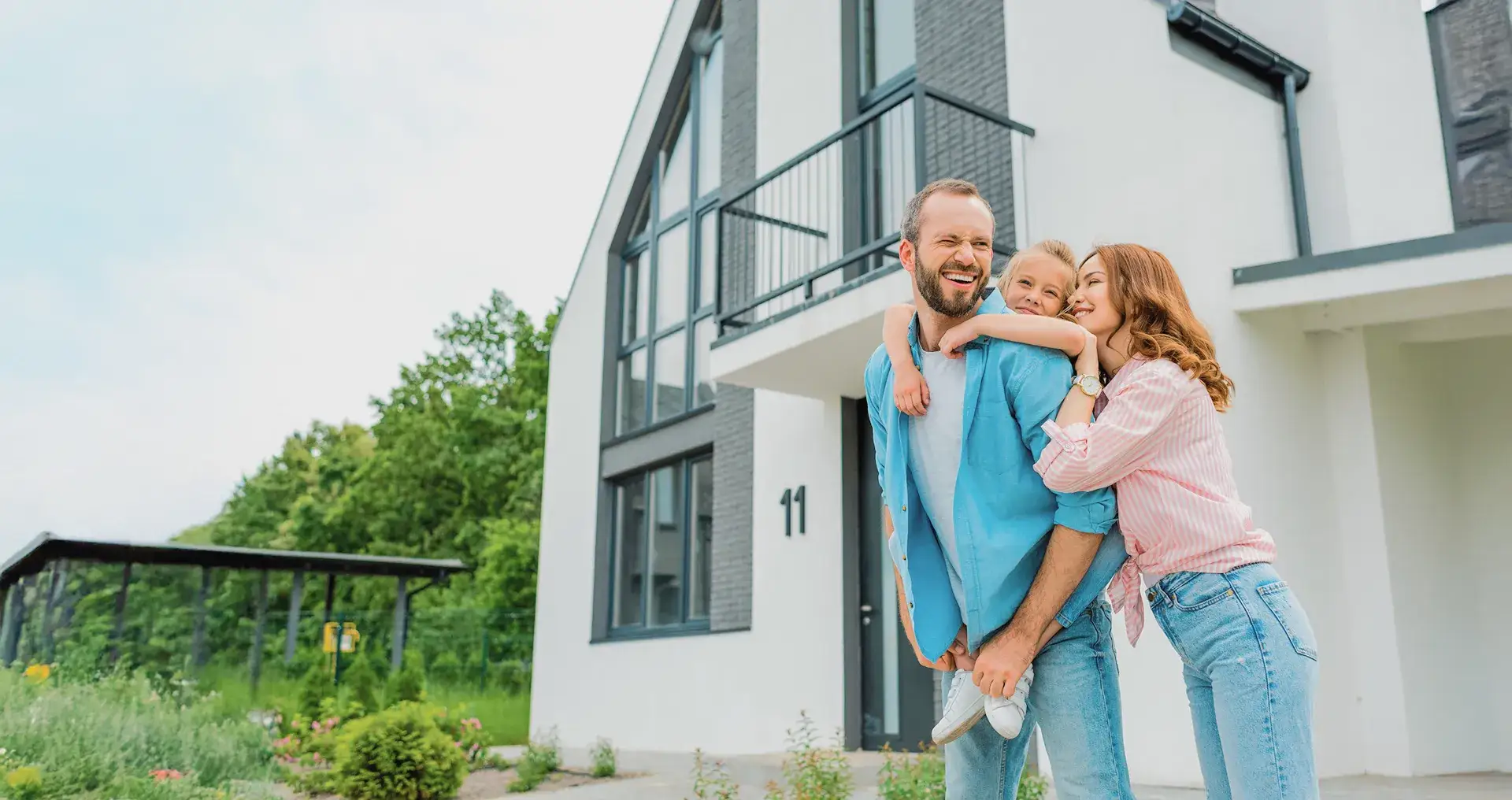 Gezin poseert lachend voor een moderne woning met carport