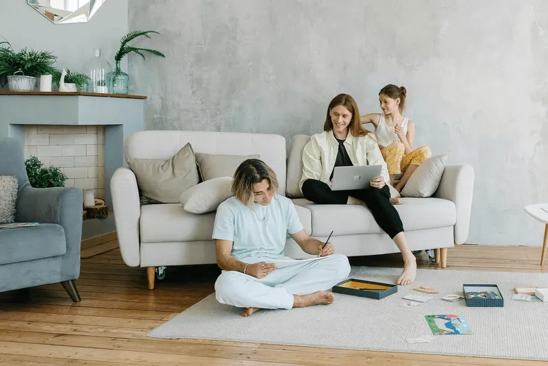 Gezin ontspant in een lichte woonkamer: man schrijft op de vloer, vrouw en dochter op de bank met tablet