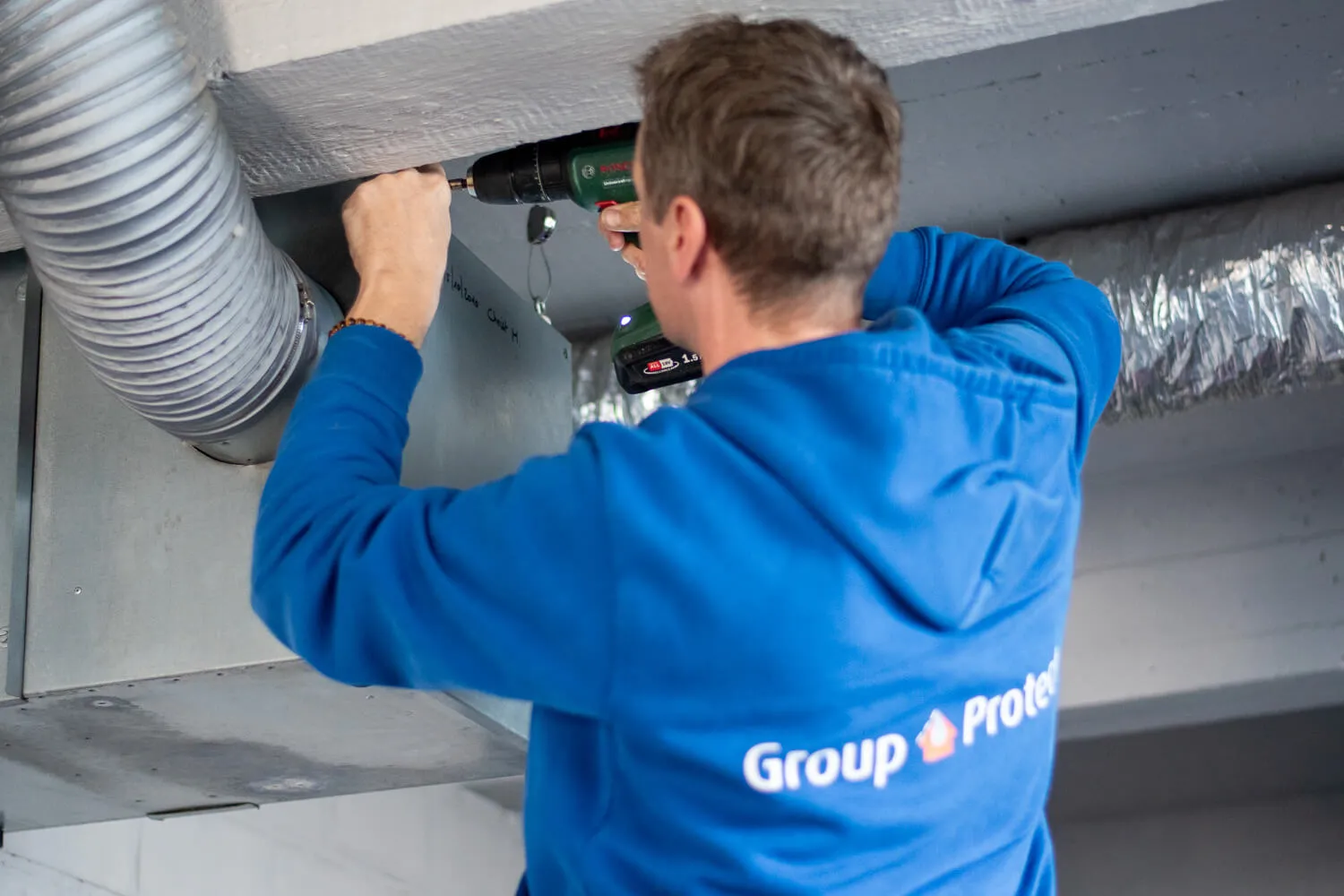 Monteur van Group Protect monteert een ventilatiekanaal tegen het plafond