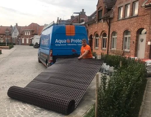 Vakman van Aqua Protect rolt een drainagefolie uit naast de bestelwagen voor een rijwoning
