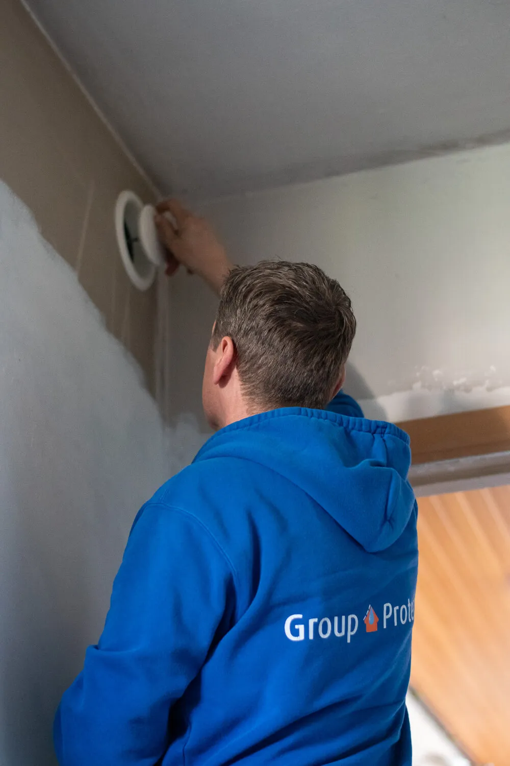 Vakman van Aqua Protect plaatst een rond ventilatierooster in de muur