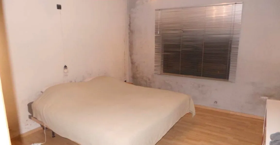 Slaapkamer met donkere vochtplekken en schimmel op de muur rond het raam