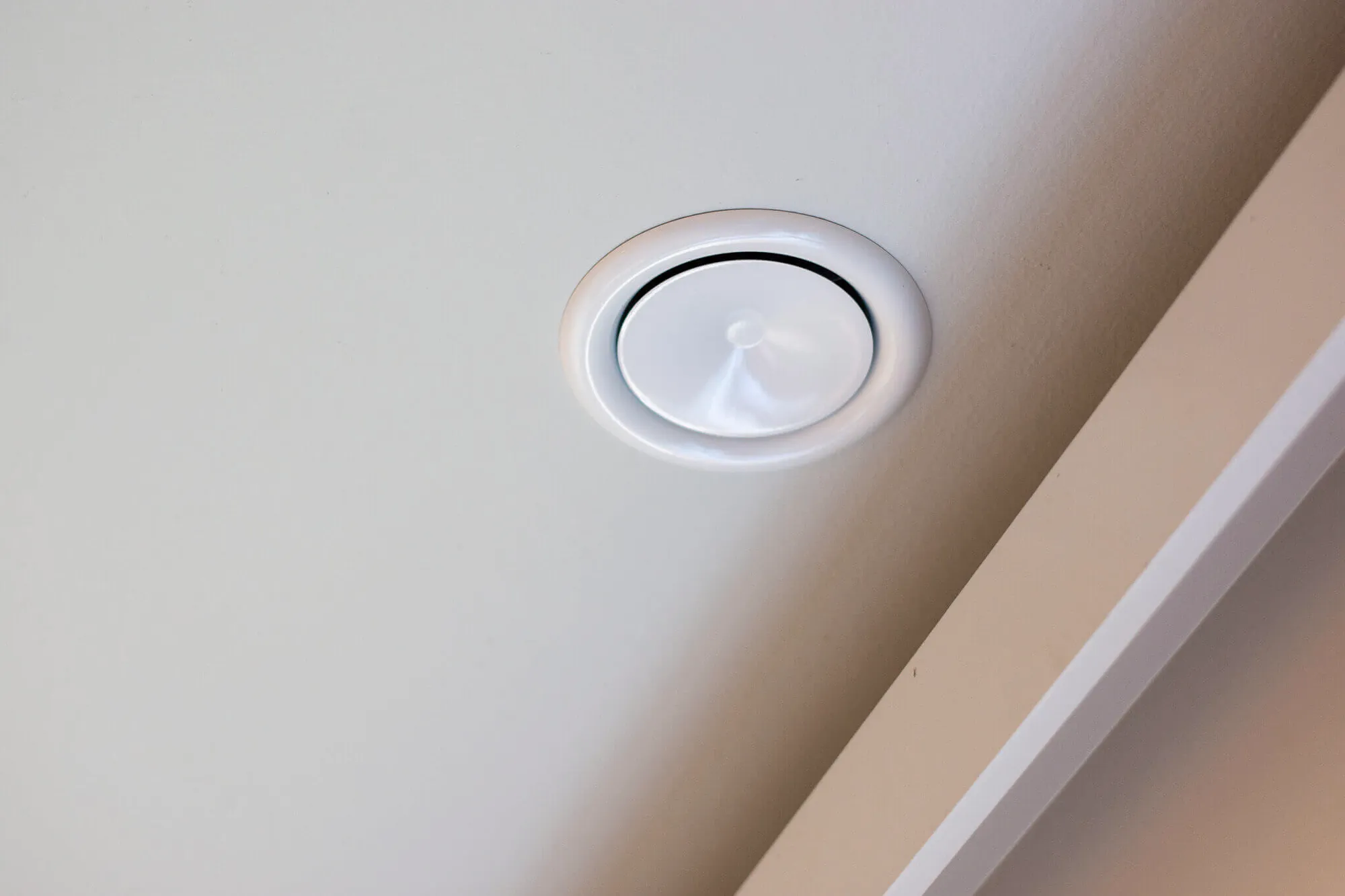 Rond wit ventilatierooster ingebouwd in een plafond bij de muurovergang