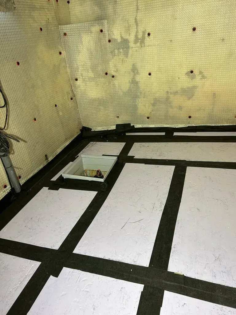 Keldervloer met isolatieplaten, drainagestroken en een pompput tijdens vloerdrainage