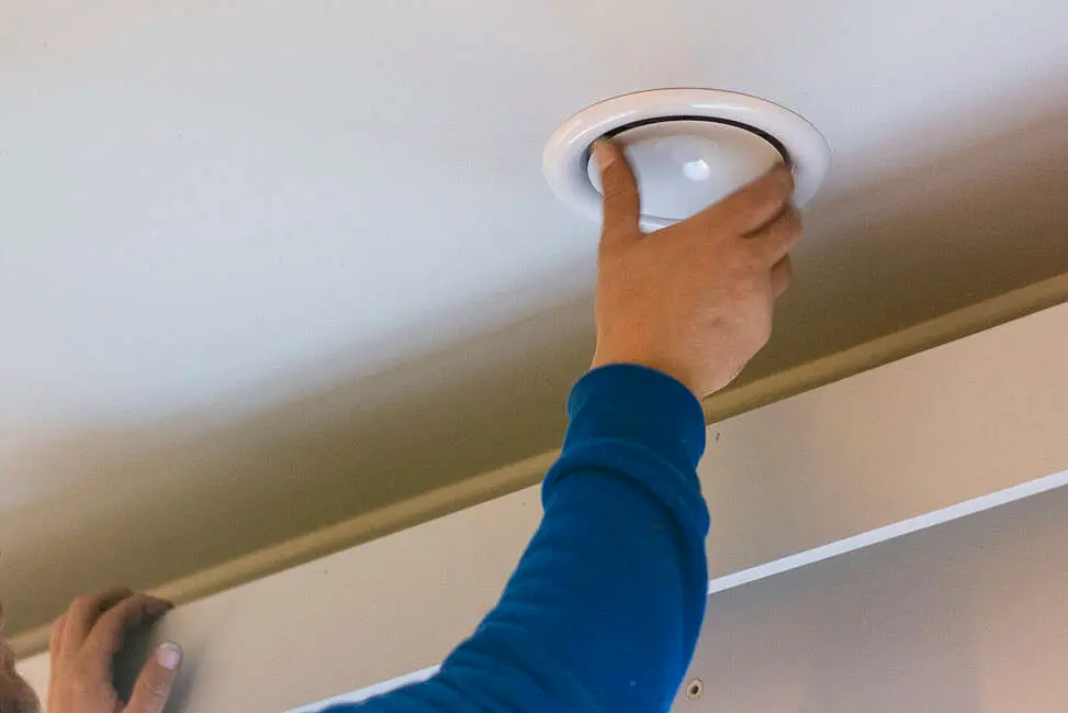 Monteur in blauwe trui plaatst een ventilatieventiel of inbouwspot in een plafond