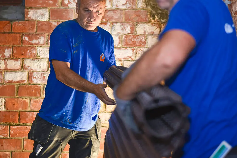 Vakman van Aqua Protect draagt een rol bitumen langs een bakstenen muur in een kelder