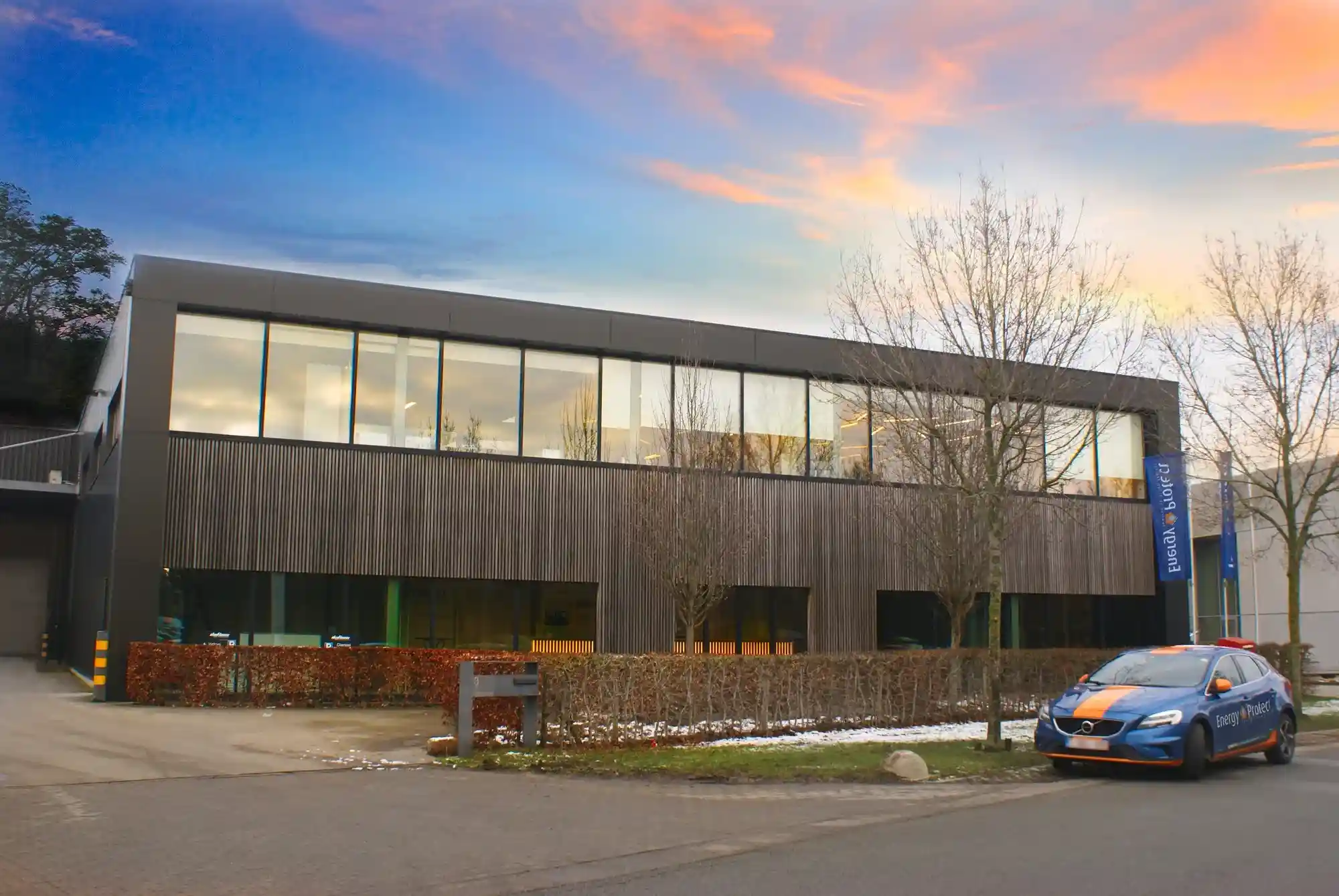 Bedrijfsgebouw van Group Protect met houten gevel bij zonsondergang, met een oranje Energy Protect-bedrijfswagen ervoor