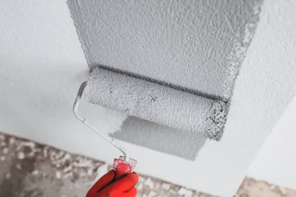 Grijze coating wordt met een verfrol op een muur aangebracht, hand met rode handschoen