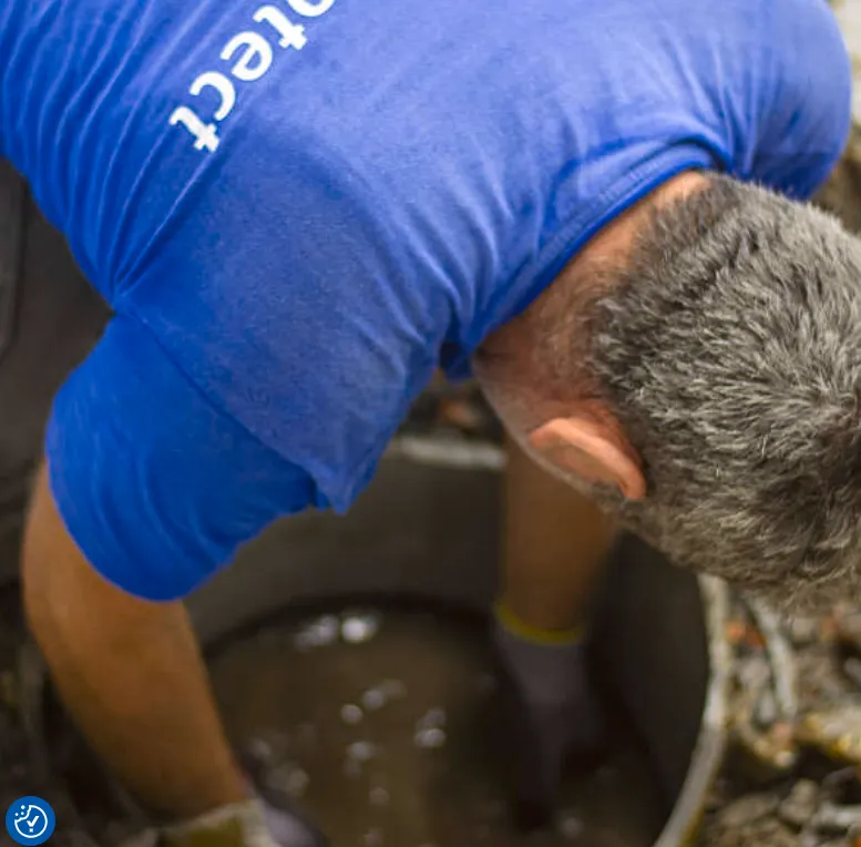 Vakman van Aqua Protect in blauwe polo gebogen over een put tijdens vochtwerk