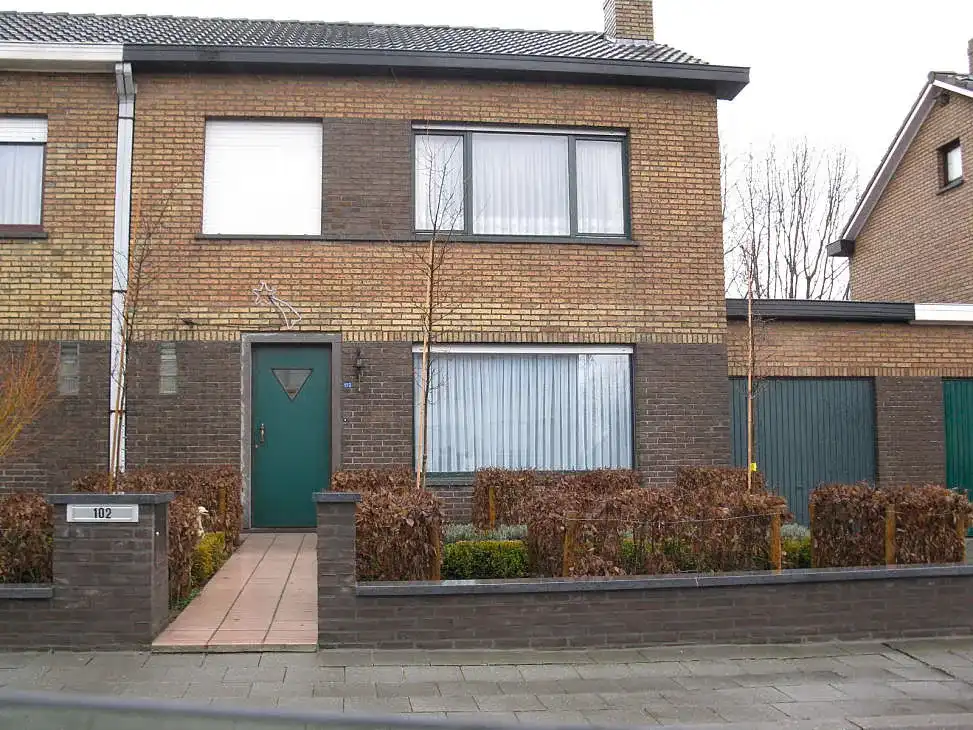 Bakstenen rijwoning met groene voordeur en oprit langs de straat