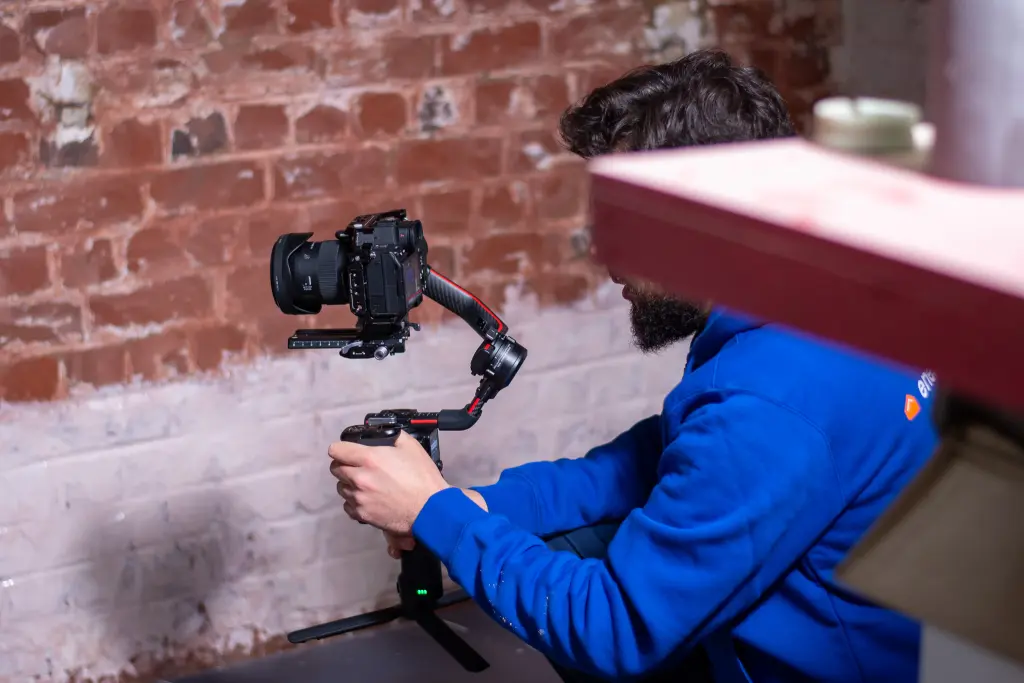 Persoon in blauwe trui filmt met een camera op gimbal een bakstenen muur tijdens een opname