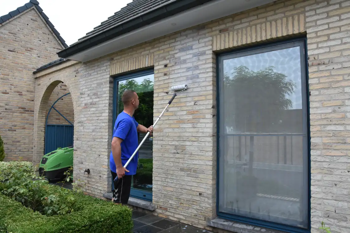 Vakman reinigt de bakstenen gevel van een woning met een telescoopborstel