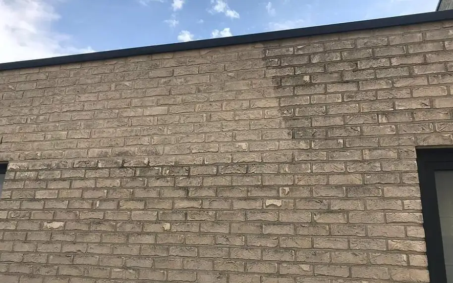 Bakstenen muur met donkere vochtaanslag onder de dakrand, een geval voor vochtbestrijding