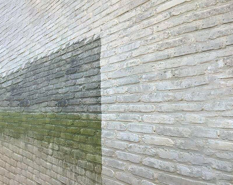 Bakstenen gevel half gereinigd: links groene aanslag, rechts een proper proefvlak na gevelreiniging