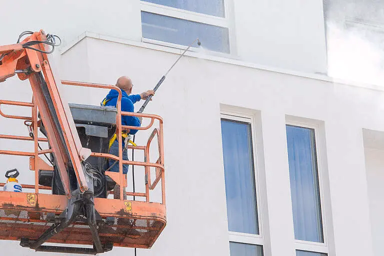 Vakman van Aqua Protect reinigt een witte gevel onder hoge druk vanuit een hoogwerker