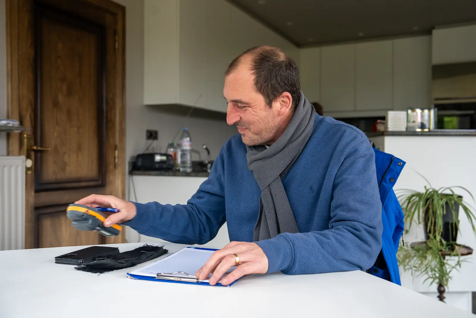 Man aan een keukentafel bekijkt een toestel met klembord tijdens een inspectie