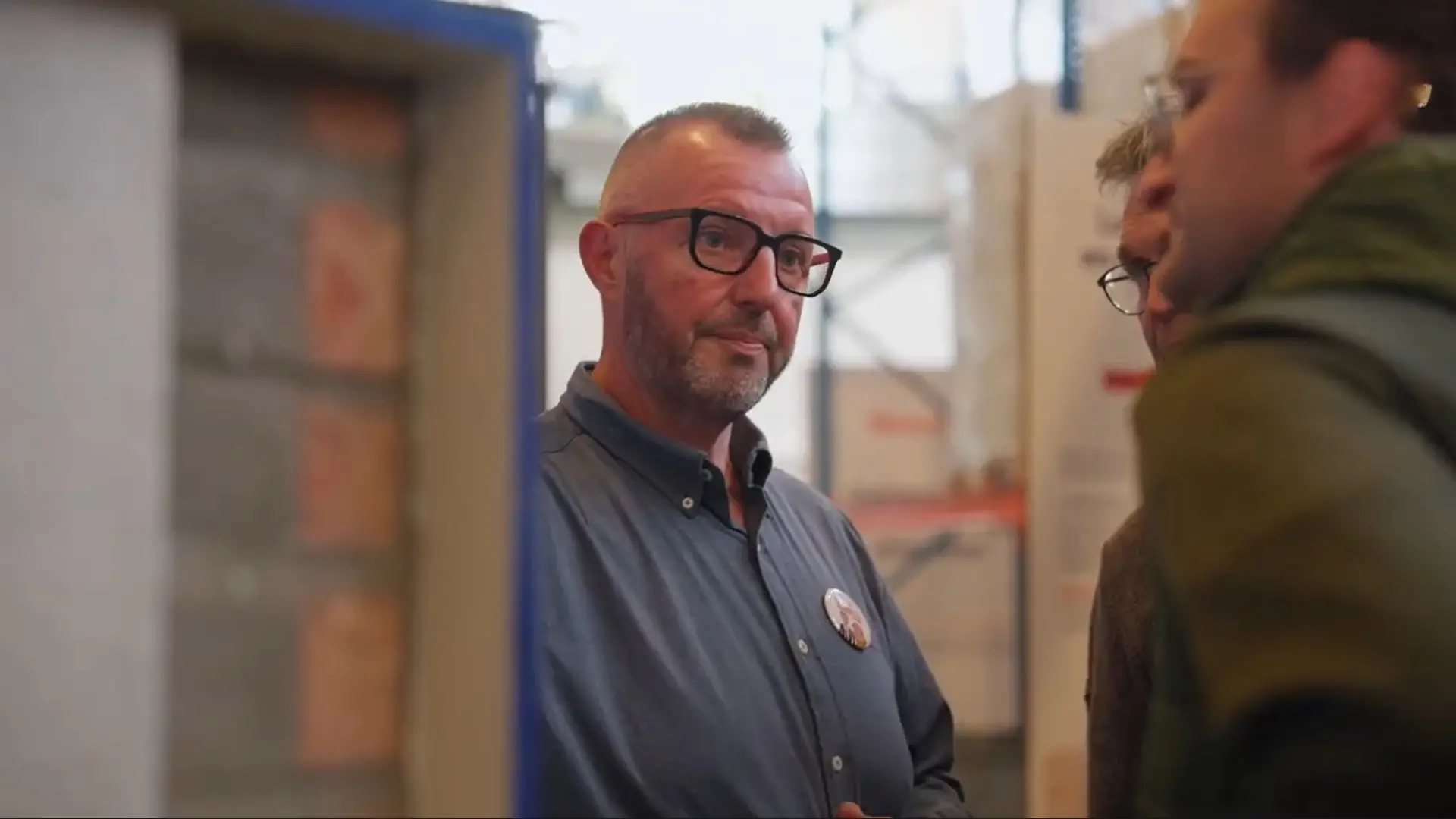Medewerker met bril in gesprek met een collega tussen de magazijnrekken