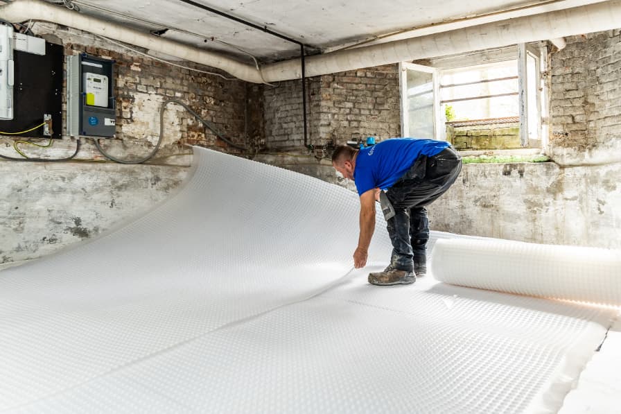 Technicien d'Aqua Protect déroule une membrane à picots blanche sur le sol d'une cave