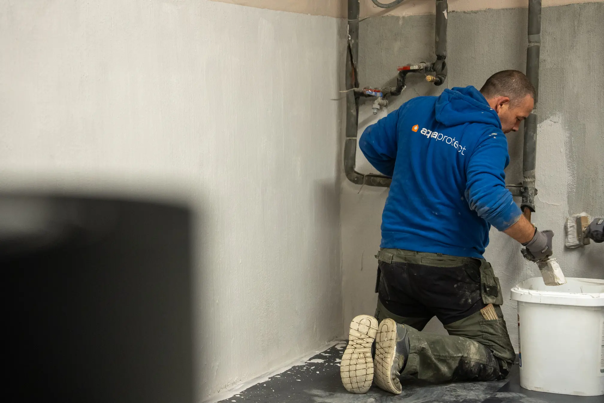 Technicien d'Aqua Protect applique un mortier d'étanchéité sur un mur de cave