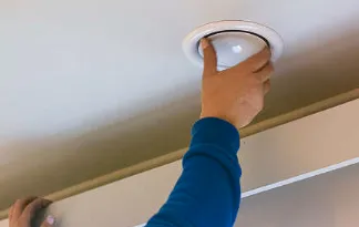Une main visse une bouche de ventilation ronde dans un plafond