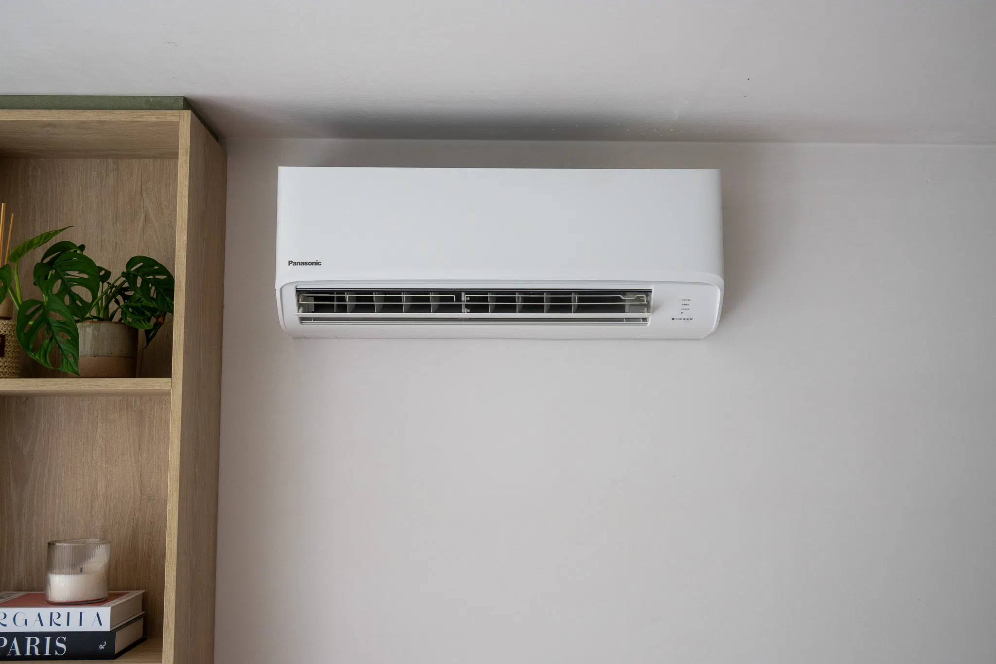 Climatiseur split blanc au mur d'un salon, à côté d'une étagère en bois