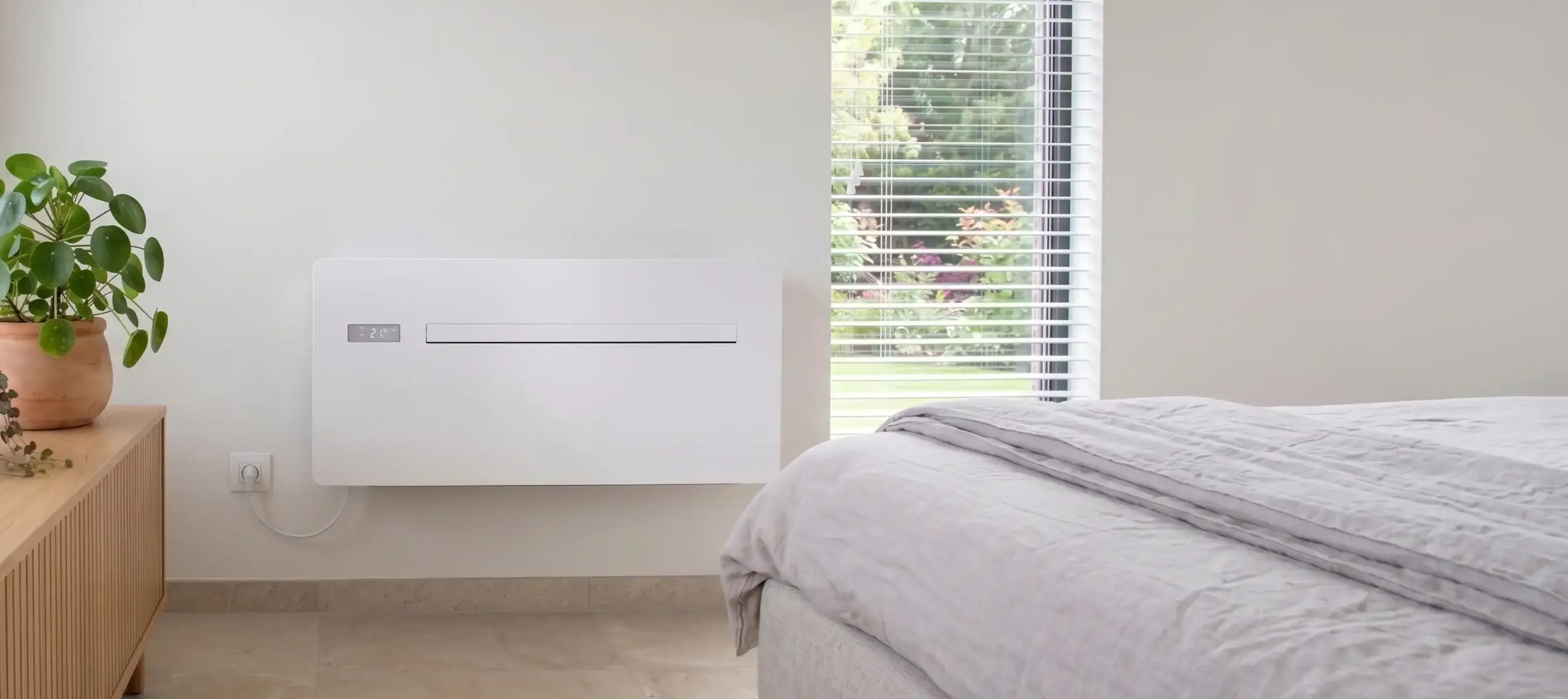 Climatiseur blanc au mur d'une chambre, à côté d'un lit et d'une plante