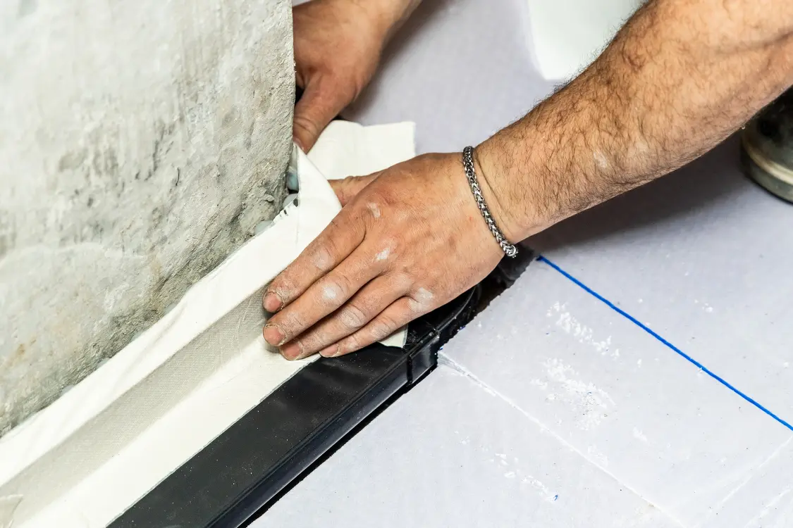 Des mains pressent une bande d'étanchéité dans l'angle entre le mur et le sol d'une cave